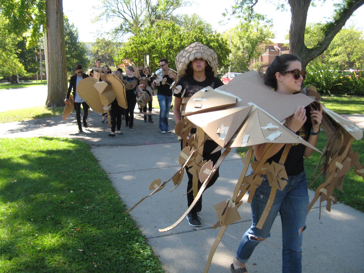 students parading in wearable cardboard sculptures