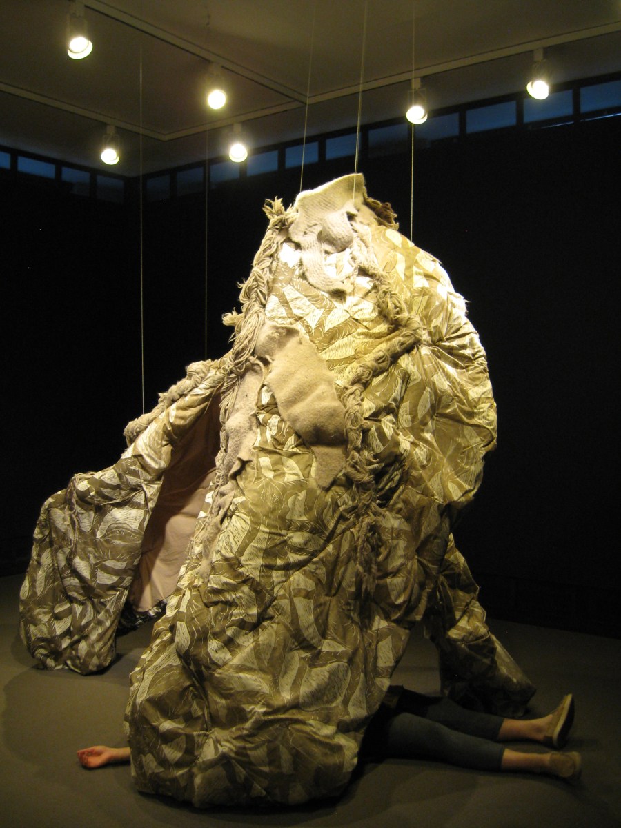 Lena lying splayed on the floor under xyr sculpture