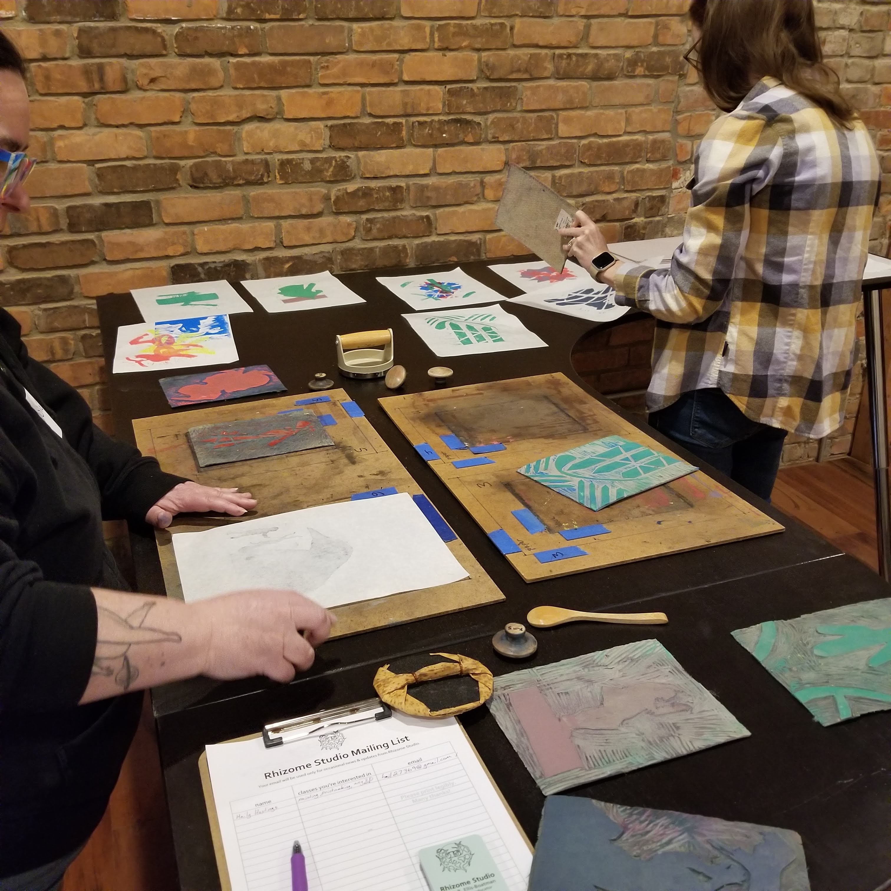 photo of hand-printing workspace with two people and many prints