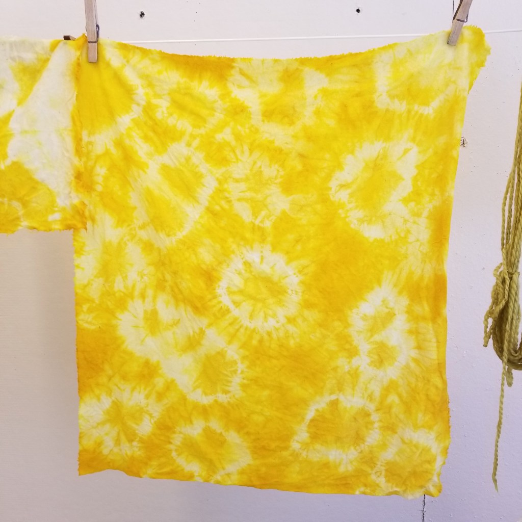 bright yellow dyed cloth with tie-dye "starburst" design; cloth is hanging from clothesline to dry